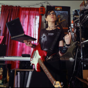 Me posing with a guitar, a laptop, and a plastic laser pistol in front of music gear and a poster of Buckaroo Banzai