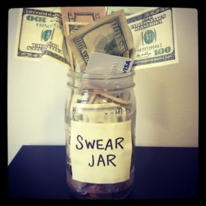 A jar labelled "swear jar" and filled with large denominations of money and a credit card