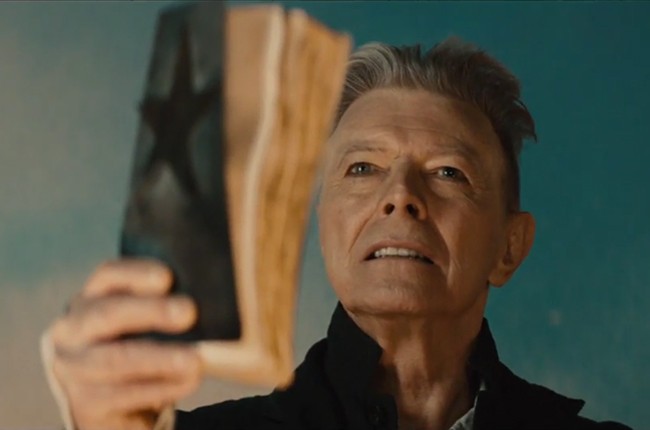 David Bowie in the Blackstar video, holding up a battered book with a black star on the cover