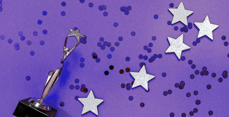 Purple backdrop with darker purple confetti on it. A trophy shaped like a person holding a star lies on it next to 5 silver stars